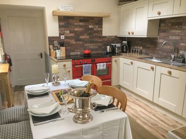 A kitchen with a red stove, beige cabinets, a dining table set with plates and a champagne bottle at Rhydlandgoed Stepaside near Saundersfoot