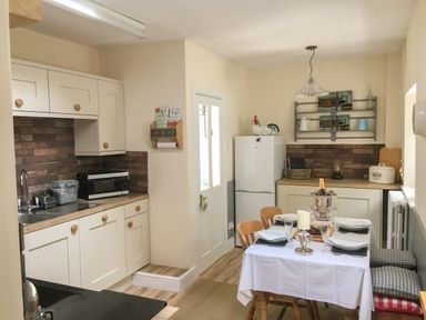 A kitchen with white cabinets a dining table set with plates and glasses and a refrigerator with a rooster on top at Rhydlandgoed Stepaside near Saundersfoot