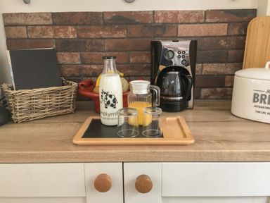 A kitchen countertop with a coffee maker a basket with books a bread container and a tray with a milk bottle a jug of juice and two glasses at Rhydlandgoed in Stepaside near Saundersfoot