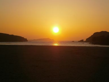 A sunset over the sea with a beach in the foreground and hills on both sides at Sunset View in Porth