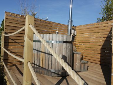An outdoor wooden hot tub with a chimney and small steps on a wooden deck with rope railing at Sunset View in Porth