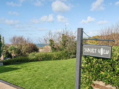 A sign for Sunset View near grass and trees in Porth