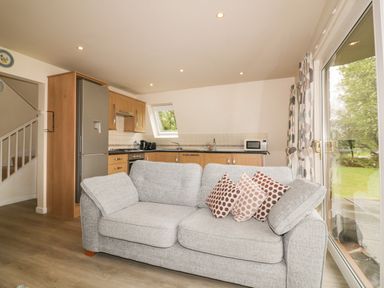 A living room with a gray sofa and pillows next to a kitchen with wooden cabinets and a window at Lodge 22 Bodmin Holiday Park Cornwall Lanivet