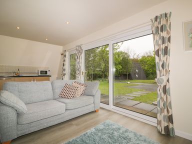 A living room with a gray sofa and patterned curtains by large glass sliding doors showing a garden outside at Lodge 22 Bodmin Holiday Park Cornwall Lanivet
