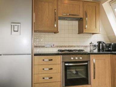 A kitchen with wooden cabinets a gas stove an oven a refrigerator and kitchen appliances on the counter at Lodge 22 Bodmin Holiday Park Cornwall