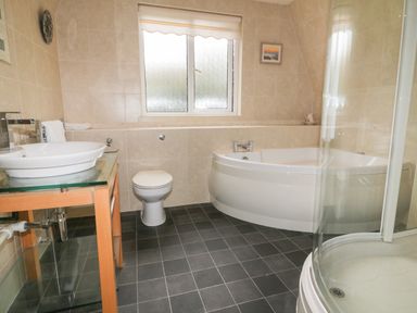 A bathroom with a corner bathtub a toilet a glass shower and a sink on a wooden stand at Lodge 22 Bodmin Holiday Park Cornwall in Lanivet