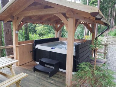 A wooden gazebo with a hot tub and steps surrounded by trees and a wooden fence at Lady Bagots Cabin in Ruthin