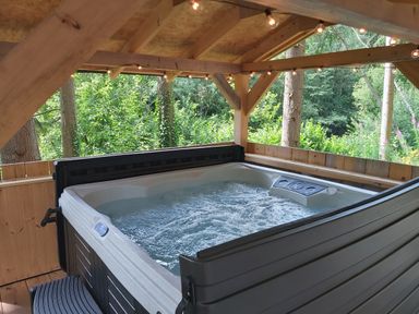 A bubbling hot tub under a wooden gazebo surrounded by trees at Lady Bagots Cabin in Ruthin
