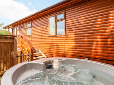 A hot tub with bubbling water next to wooden steps and a log cabin exterior at Callow Lodge 22 in Beaconsfield Holiday Park