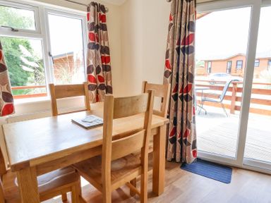 A dining area with a wooden table and chairs near windows and sliding glass door at Callow Lodge 22 in Beaconsfield Holiday Park