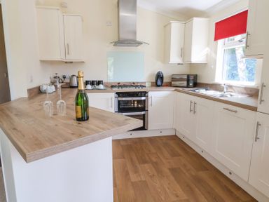 A kitchen with white cabinets a wooden countertop a bottle and two glasses on the counter at Callow Lodge 22 Beaconsfield Holiday Park