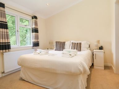 A bedroom with a double bed two bedside tables and a window with striped curtains at Callow Lodge 22 Beaconsfield Holiday Park