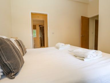 A bedroom with a bed pillows and folded towels facing an open door to a bathroom and another open door at Callow Lodge 22 Beaconsfield Holiday Park