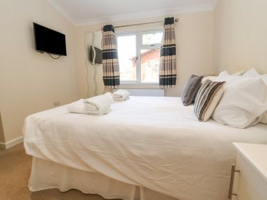 A bedroom with a bed made with white bedding two folded towels a wall-mounted tv striped curtains and a window at Callow Lodge 22 Beaconsfield Holiday Park