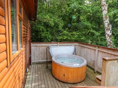 An outdoor wooden deck area with a hot tub next to a log cabin at Callow Lodge 22 in Beaconsfield Holiday Park