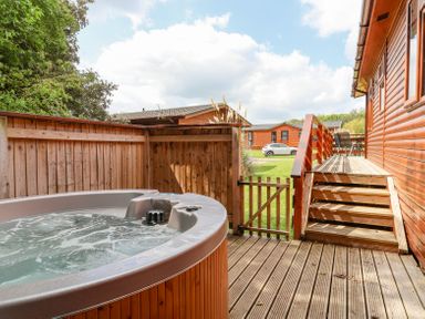 An outdoor hot tub on a wooden deck next to a wooden fence and steps leading up to a porch at Callow Lodge 22 in Beaconsfield Holiday Park