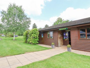 A wooden reception building with a paved walkway and green grass at Beaconsfield Holiday Park