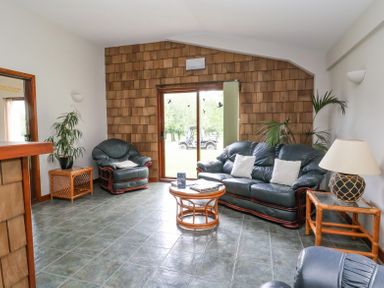 A living room with leather sofas a round wooden coffee table plants and sliding glass doors at Callow Lodge 22 in Beaconsfield Holiday Park