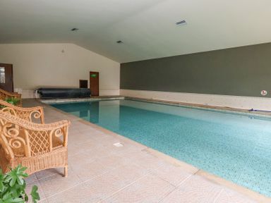An indoor swimming pool with wicker chairs and tiled flooring at Callow Lodge 22 Beaconsfield Holiday Park
