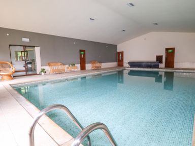 An indoor swimming pool with metal handrails and wicker chairs along the wall at Callow Lodge 22 in Beaconsfield Holiday Park