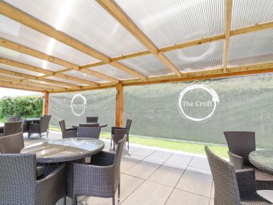 An outdoor seating area with round tables and wicker chairs under a wooden pergola at Callow Lodge 22 Beaconsfield Holiday Park