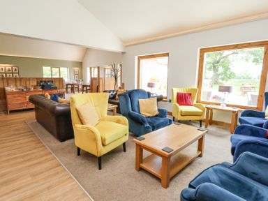 A sitting area with yellow and blue armchairs around a wooden coffee table in a room with large windows at Callow Lodge 22 in Beaconsfield Holiday Park