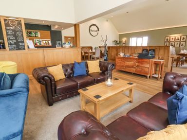 A lounge area with leather sofas and a wooden coffee table near a bar at Callow Lodge 22 in Beaconsfield Holiday Park
