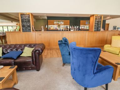 A lounge area with leather and fabric armchairs and sofas facing a wooden bar with bottles and chalkboard menus at Callow Lodge 22 Beaconsfield Holiday Park
