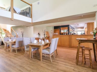A dining area with wooden tables and upholstered chairs and a wooden bar at Callow Lodge 22 Beaconsfield Holiday Park