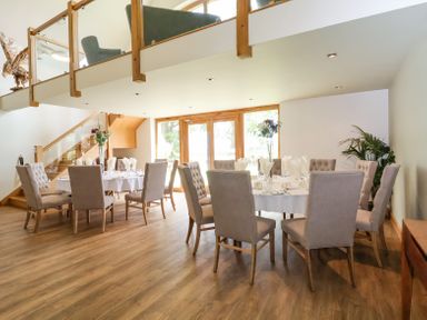 A dining room with two round tables set with napkins and glasses and beige chairs at Callow Lodge 22 in Beaconsfield Holiday Park