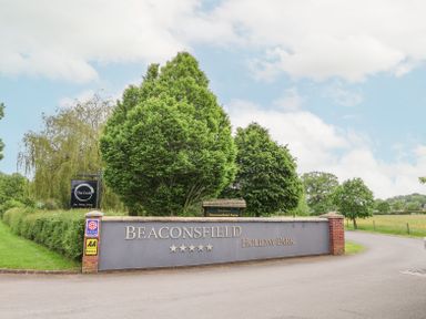 Entrance sign for Beaconsfield Holiday Park with trees and a road