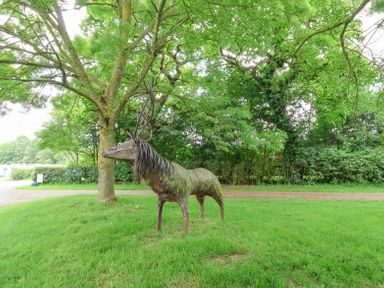 A metal sculpture of a deer on grass with trees and bushes in the background at Callow Lodge 22 in Beaconsfield Holiday Park