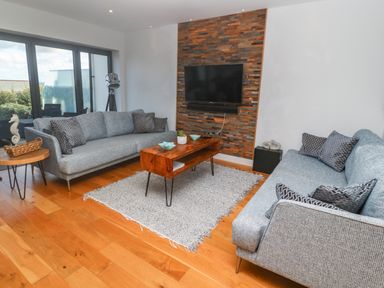 A living room with two gray sofas a wooden coffee table a gray rug and a wall-mounted television at Seafield in Carbis Bay near St Ives