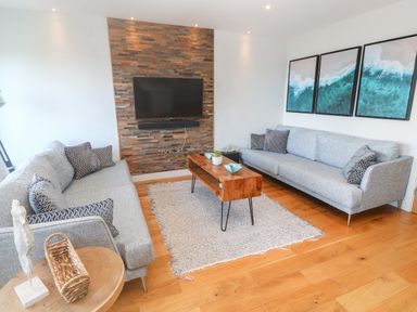 A living room with two gray sofas a wooden coffee table and a wall-mounted TV at Seafield in Carbis Bay near St Ives