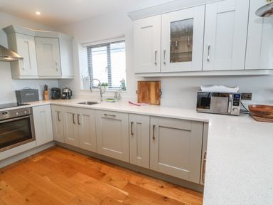 A kitchen with grey cabinets white countertops a stainless steel oven microwave and wooden floor at Seafield in Carbis Bay near St Ives