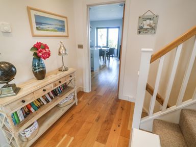 A hallway with wooden floor a staircase and a console table with books lamp and vase at Seafield Carbis Bay near St Ives