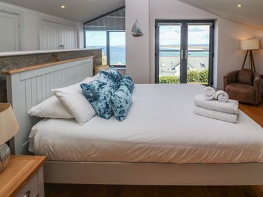 A bedroom with a bed with blue pillows and folded towels by a window overlooking the sea at Seafield in Carbis Bay near St Ives