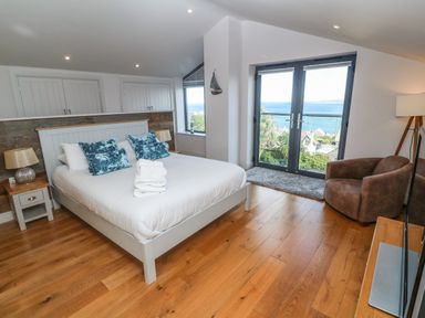 A bedroom with a bed side tables armchair and double doors overlooking the sea at Seafield in Carbis Bay near St Ives