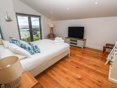 A bedroom with a bed towels on the bed a television on a stand a chair and wooden flooring at Seafield in Carbis Bay near St Ives