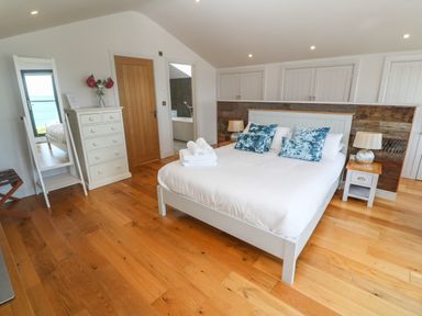A bedroom with a white bed blue pillows wooden floor and a mirror at Seafield in Carbis Bay near St Ives