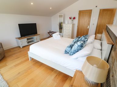 A bedroom with a bed with pillows folded towels dresser mirror and television at Seafield in Carbis Bay near St Ives