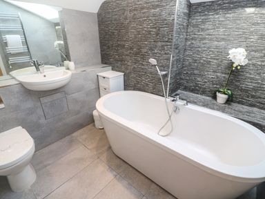 A bathroom with a white bathtub, sink, toilet, and a small cabinet with a potted plant at Seafield in Carbis Bay near St Ives