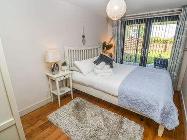 A bedroom with a bed pillows and folded towels bedside table lamps and a glass door leading to a garden at Seafield in Carbis Bay near St Ives