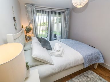A bedroom with a bed with pillows and folded towels near glass sliding doors with vertical blinds at Seafield in Carbis Bay near St Ives