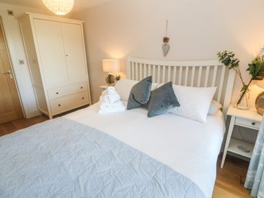 A bedroom with a white bed frame and blue pillows with white wardrobes and bedside tables at Seafield in Carbis Bay near St Ives