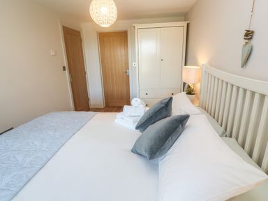 A bedroom with a bed with pillows a wardrobe two wooden doors and a lamp at Seafield in Carbis Bay near St Ives