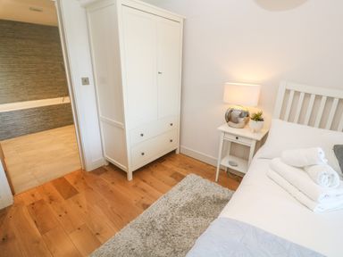 A bedroom with a white wardrobe a bedside table with a lamp and towels on a bed near Seafield in Carbis Bay near St Ives