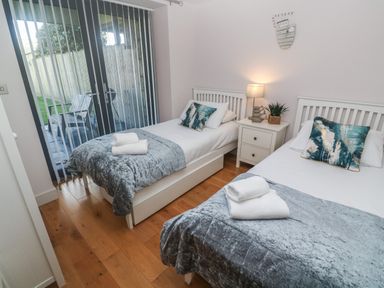 A bedroom with two single beds side by side a nightstand with a lamp and plant and glass doors leading outside at Seafield in Carbis Bay near St Ives