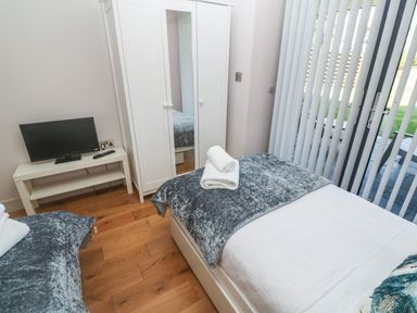 A bedroom with two single beds a white wardrobe and a TV on a small table at Seafield in Carbis Bay near St Ives
