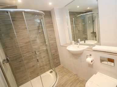 A bathroom with a glass shower enclosure a wall-mounted sink a mirror and a toilet at Seafield in Carbis Bay near St Ives